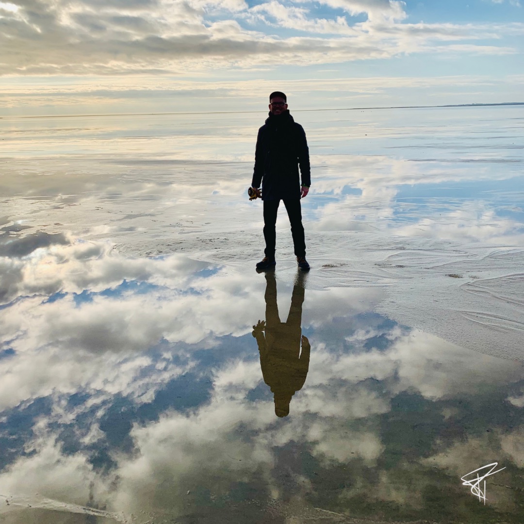 Spektakuläres Foto einer sich spiegelnden Wasserlandschaft mit Wolken, darauf ein standfest stehender Mann. Impulse von Ralf Tiedemann - Klang. Wort. Sinn.